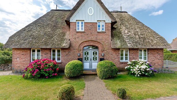 A traditional brick house with a thatched roof, a central door, and symmetrical windows.