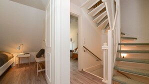 A bedroom with a bed, bedside table, chair, and a staircase leading to another room.