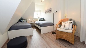 A compact bedroom with two beds, a chair, and a floor lamp.