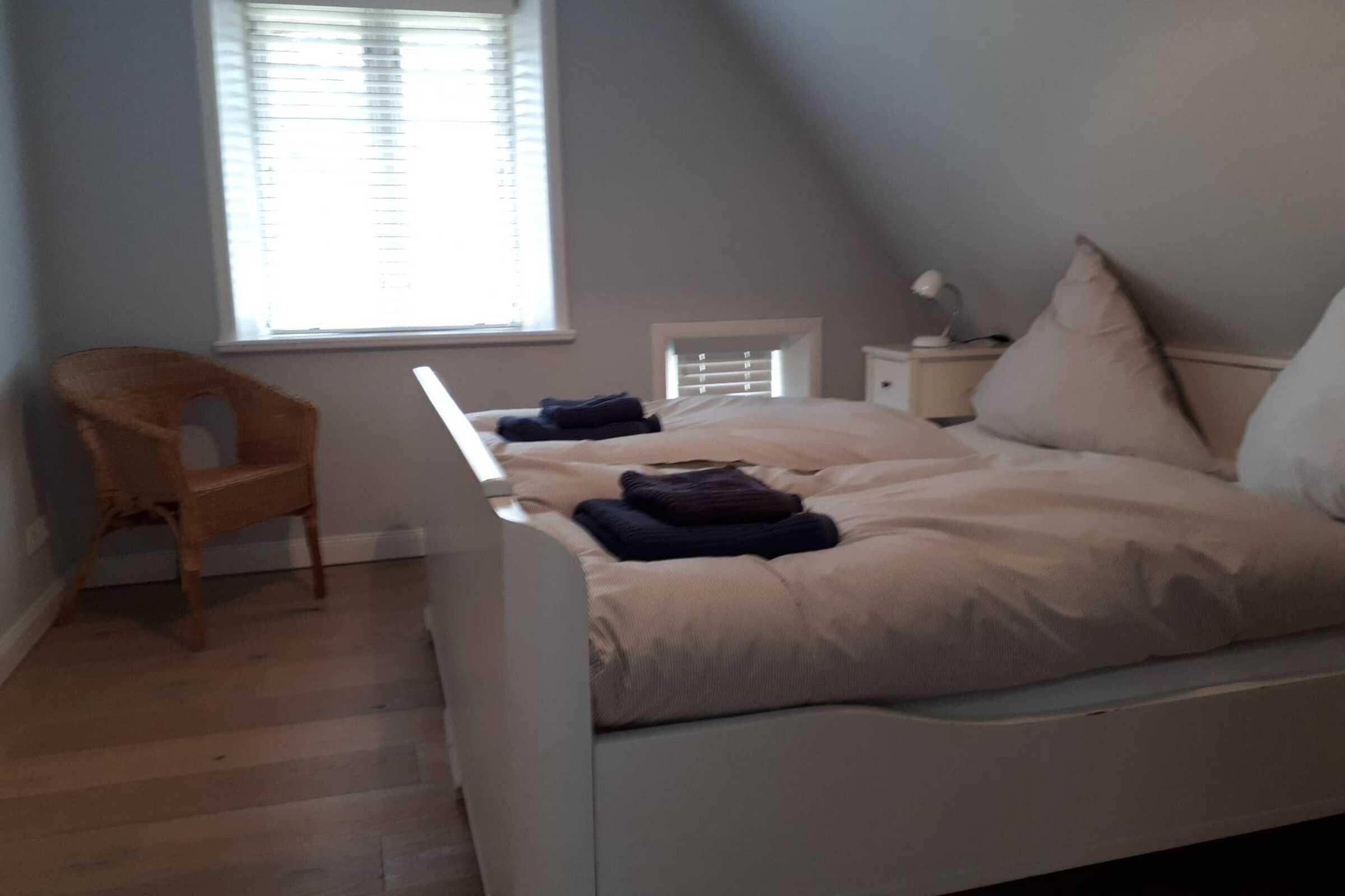 A bedroom with a bed, a chair, a nightstand, and a window with blinds.