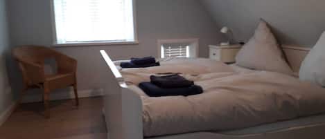 A bedroom with a bed, a chair, a nightstand, and a window with blinds.