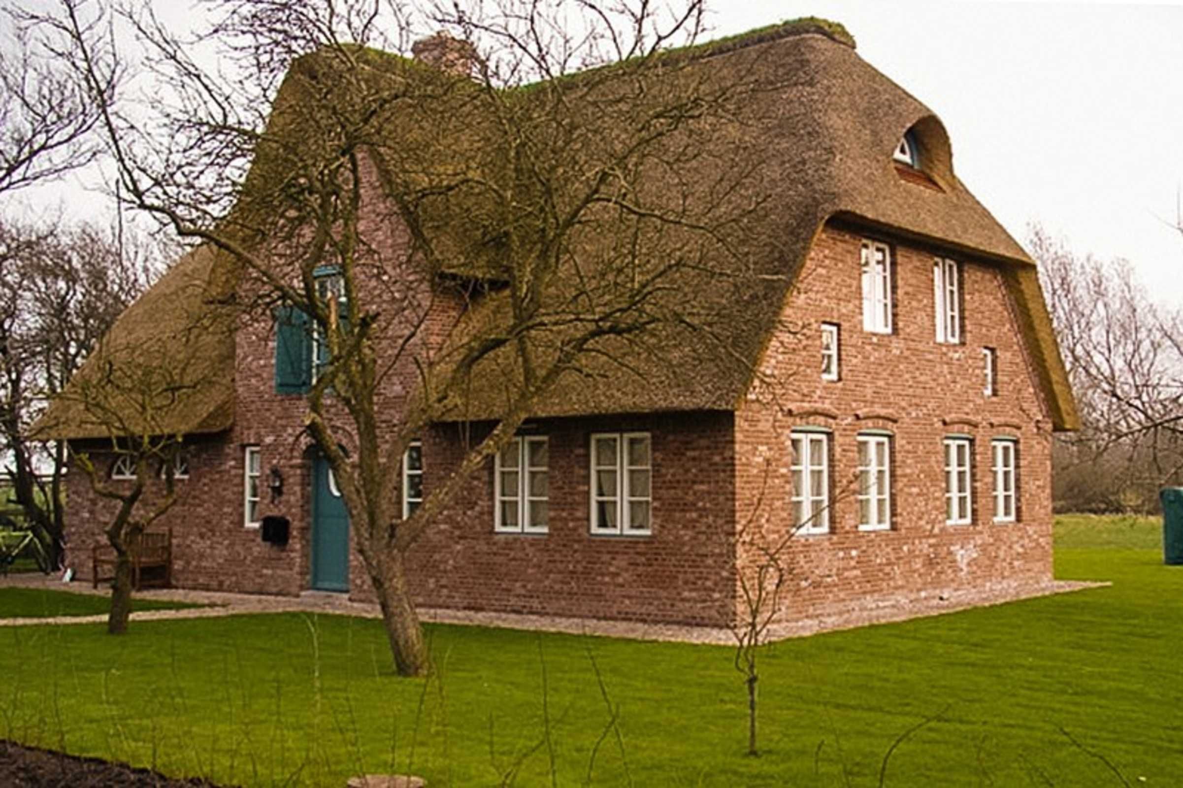 Una casa tradicional de ladrillo con tejado de paja, puerta verde y un pequeño jardín.