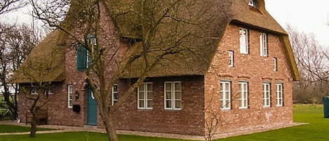 A traditional brick house with a thatched roof, a green door, and a small garden.