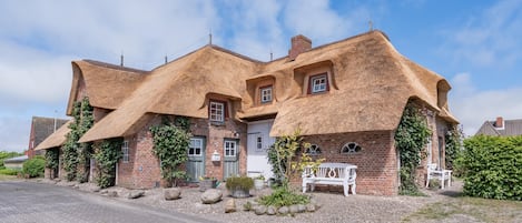 Ein traditionelles Haus mit Strohdach, Ziegelmauern, einer gepflasterten Auffahrt und einer weißen Bank.