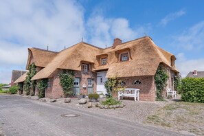 Une maison traditionnelle à toit de chaume, avec des murs en briques, une allée pavée et un banc blanc.