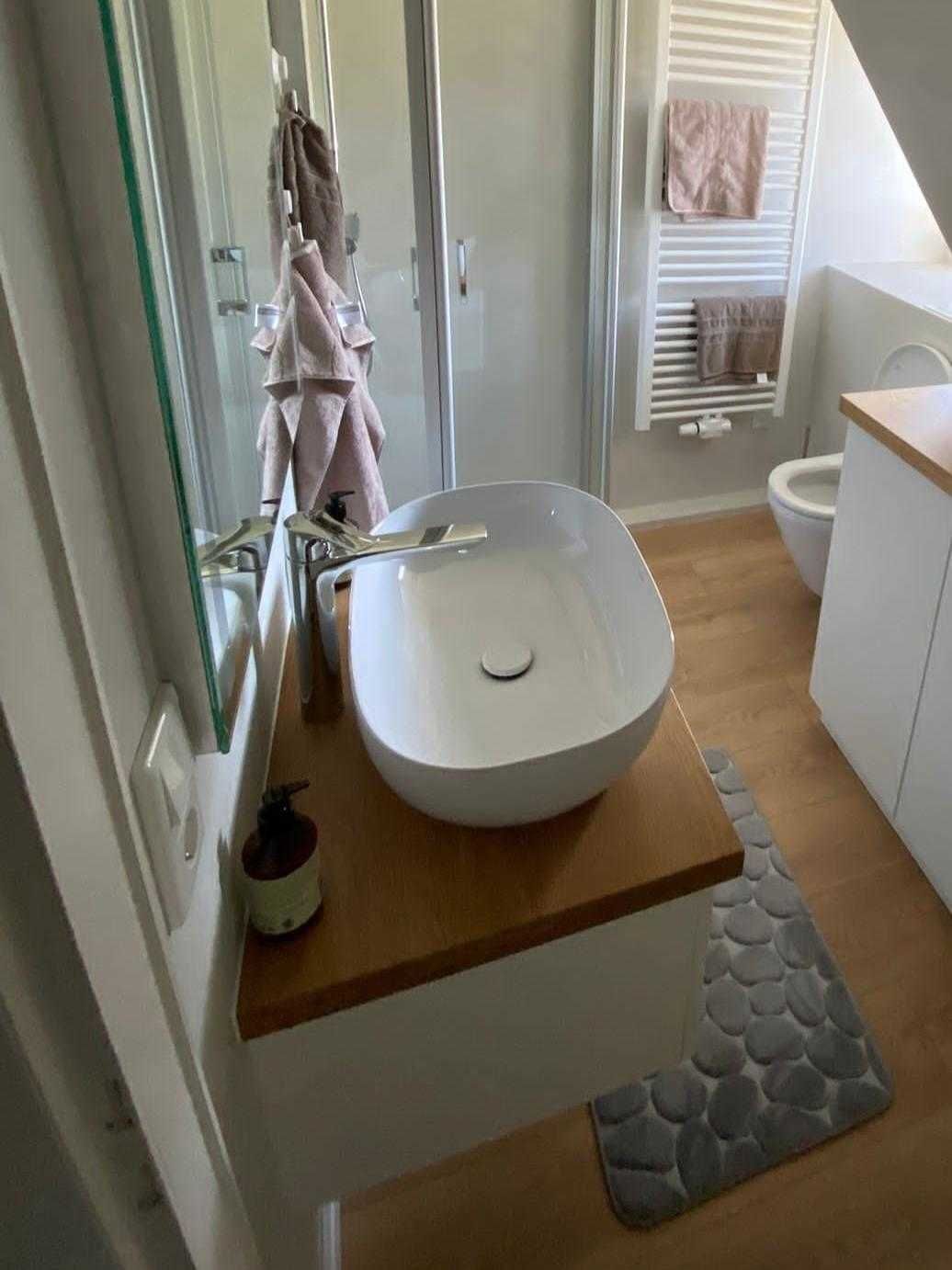 A modern bathroom with a large white sink, wooden vanity, and a stone-patterned rug.