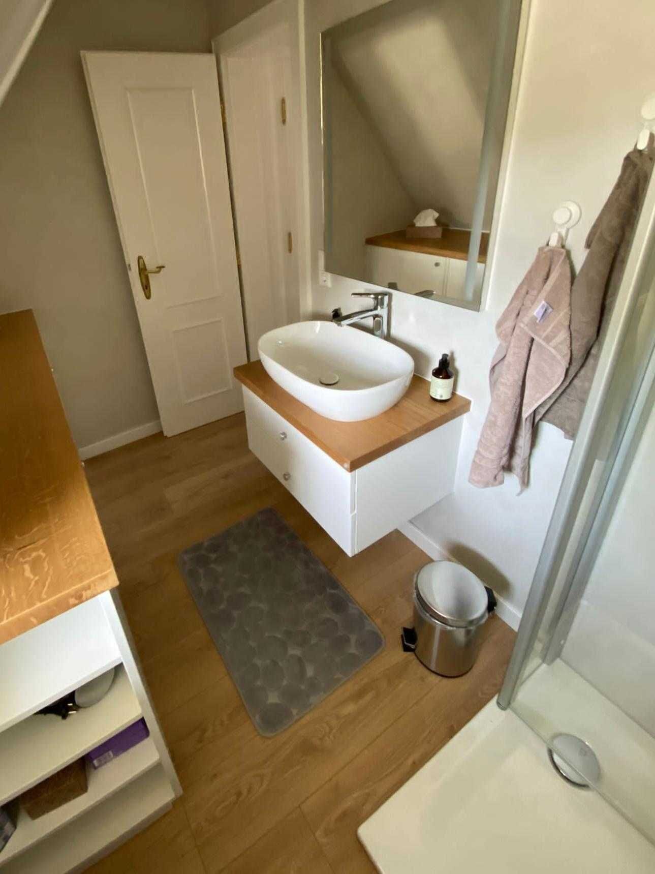 A bathroom with a white sink, wooden vanity, a mirror, a towel rack, and a shower area.
