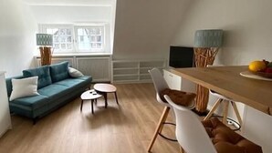 Ein modernes Wohnzimmer mit einer Couch, einem Esstisch und Stühlen. Auf dem Tisch befindet sich ein Fernseher und eine Lampe.