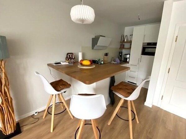 A modern kitchen with a wooden island, white chairs, and a hanging light fixture. - Hochstieg 2, Whg Busch, Nieblum* (Nieblum)