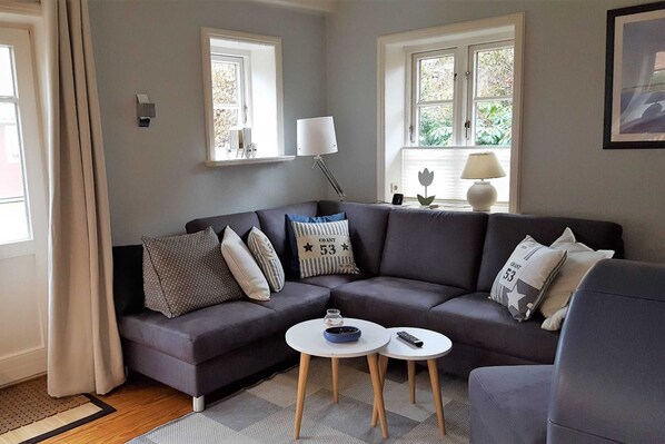 A modern living room with a grey sofa, two small round tables, and a window with curtains.
