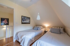 Ein Schlafzimmer mit zwei Betten, Holzboden, weißer Geländer, Nachttisch und einer Wandlampe.