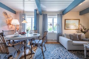 Ein Essbereich mit einem runden Tisch, Stühlen und einer Lampe. Es gibt ein Sofa und ein Gemälde an der Wand.
