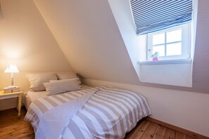 Une chambre avec un plafond en pente, une fenêtre donnant sur un beau paysage, une table de chevet avec une lampe et un lit avec une literie à rayures.