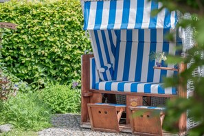 Un espace extérieur aménagé avec des sièges en bois, surmonté d’un auvent rayé bleu et blanc, et entouré d’une végétation luxuriante.