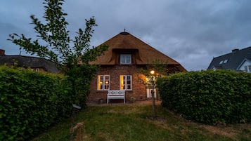 Een huis met rieten dak, een witte bank in de voortuin en een verzorgde haag.