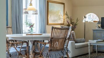 Een eetgedeelte met een ronde tafel, rieten stoelen, gestreepte kussens, een vaas met bloemen en een lamp.