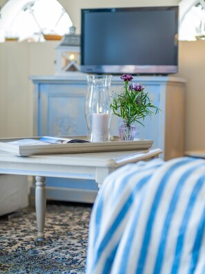 Un salon bien aménagé, avec un téléviseur, un vase en verre rempli de fleurs et un plateau sur lequel reposent un livre et une télécommande.