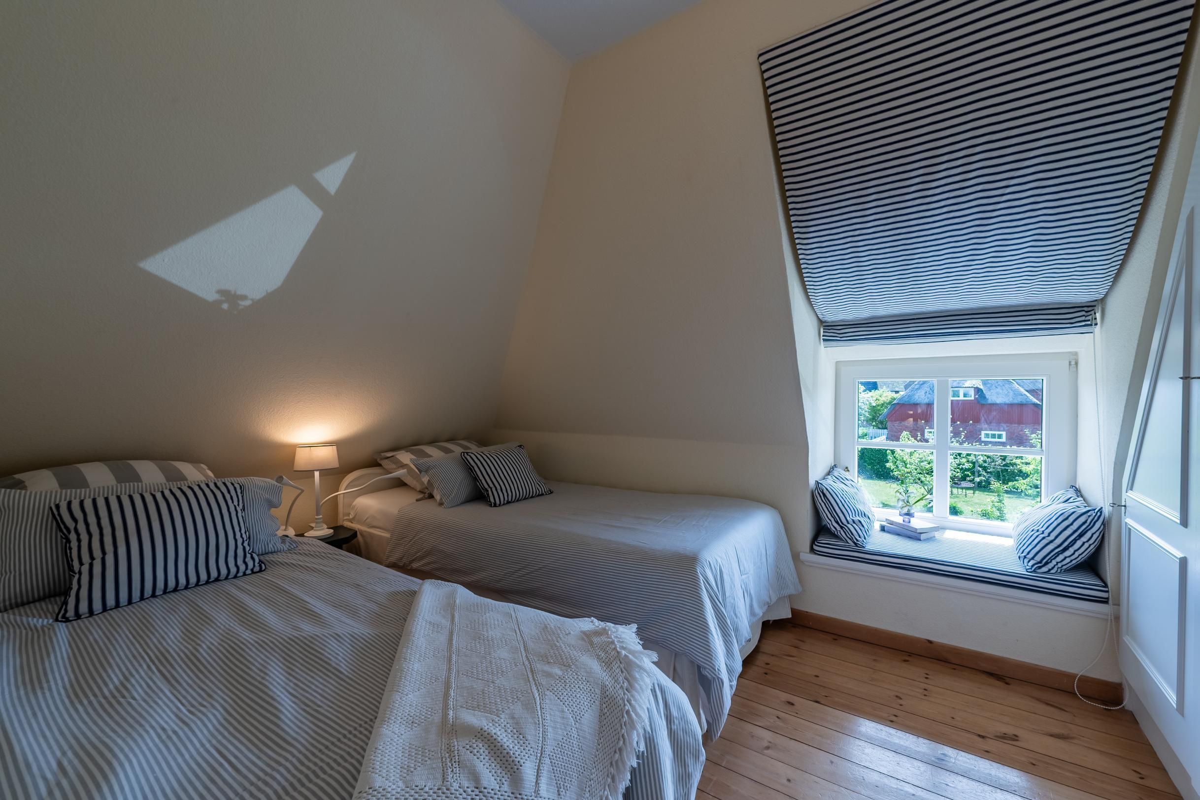 Et soveværelse med to senge, et vinduesbænk med udsigt og en projektor på væggen.