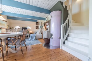 Un salon chaleureux avec un plancher en bois, une table ronde, des chaises en osier, un canapé et un escalier doté d’une rampe blanche.