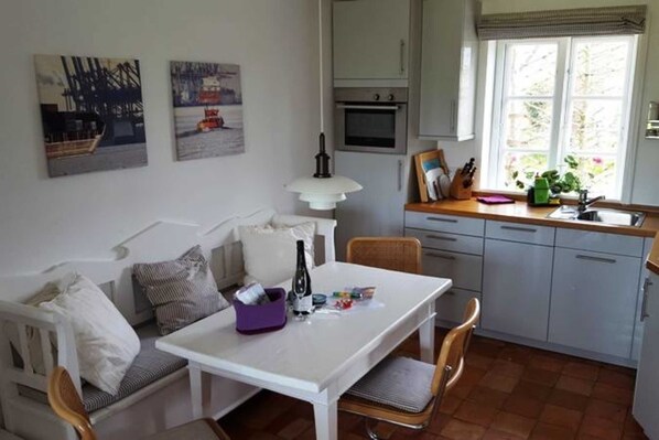 A compact kitchen with a dining area, featuring a white table, chairs, and a built-in oven. - Hüs Saaltfeen, part of the house Guatingwai 18 a - Hüs Saaltfeen, part of the house Guatingwai 18 (Nieblum)