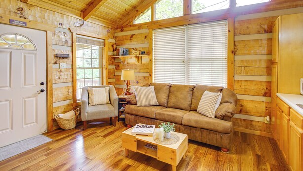 A cozy log cabin interior with a wooden floor, a brown sofa, a small armchair, and a coffee table.