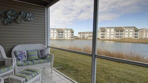 A covered patio with wicker furniture and a view of a lake and apartment buildings. - First Floor Contemporary with Top Bay View, Pool, Tennis & Free Activities Including Golf and More. (Ocean View)