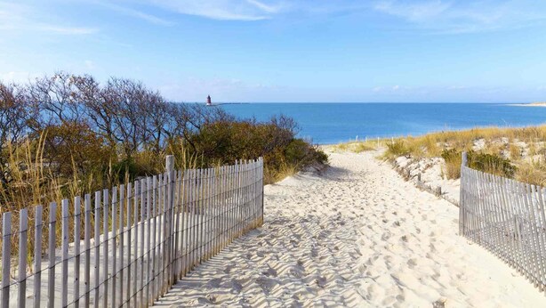 A sandy beach path leading to the ocean with a lighthouse in the distance. - First Floor Contemporary with Top Bay View, Pool, Tennis & Free Activities Including Golf and More. (Ocean View)