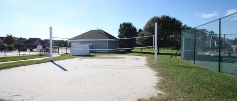 A volleyball court with a net, a small shed, and a chain-link fence.