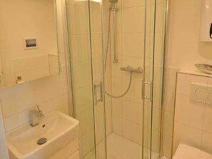 A glass-enclosed shower stall with a handheld showerhead, a sink with a mirror, and a toilet. - Kliffkoje, Guatingwai 12 Foehr (Nieblum)