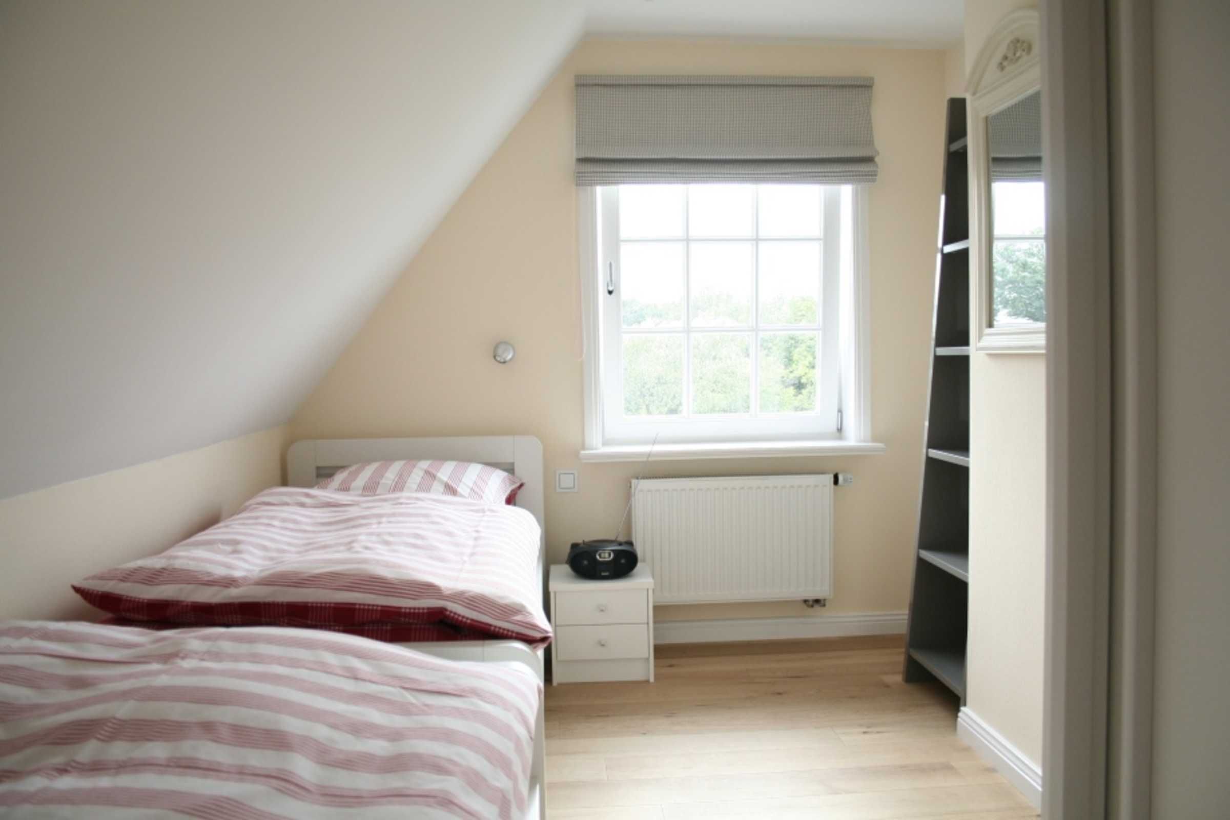 Ein Schlafzimmer mit Bett, Fenster mit Heizkörper, Nachttisch und Regalelement.