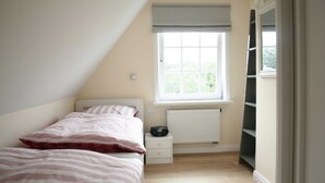 Een slaapkamer met een bed, een raam met een radiator, een nachtkastje en een wandplank.