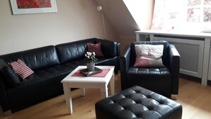 Een woonkamer met een zwarte leren bank, een zwarte lederen fauteuil en een witte salontafel met een bloevas.