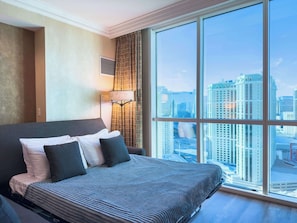 A hotel room with a large bed, a city view, and a modern lamp.
