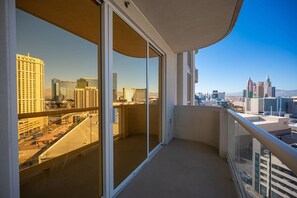 A balcony with a city view, large sliding glass doors, and a clear sky.