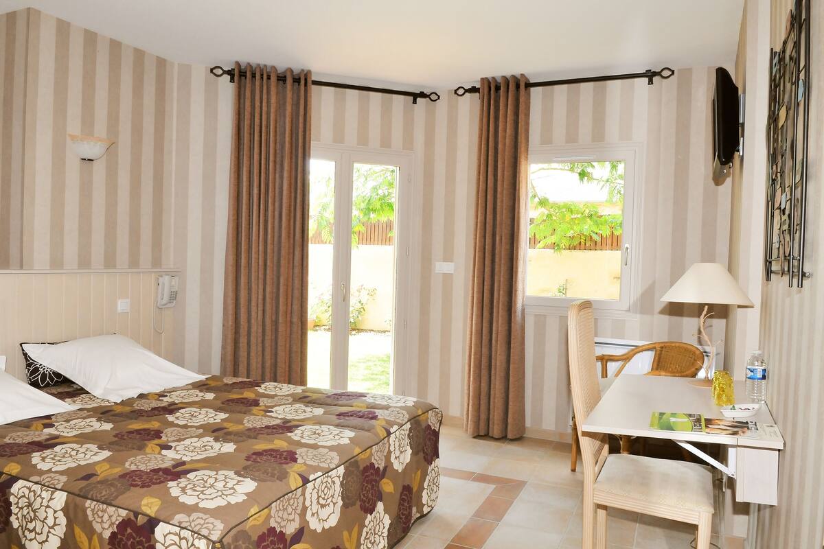 A hotel room with a bed, a desk, a chair, a lamp, and curtains.