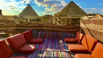 Una terraza en la azotea con un colorido tapete a rayas, asientos acolchados color naranja y vistas a las pirámides.
