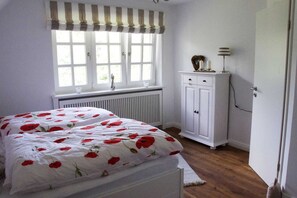 A bedroom with a bed, a radiator, a window with curtains, a cabinet, and a door.