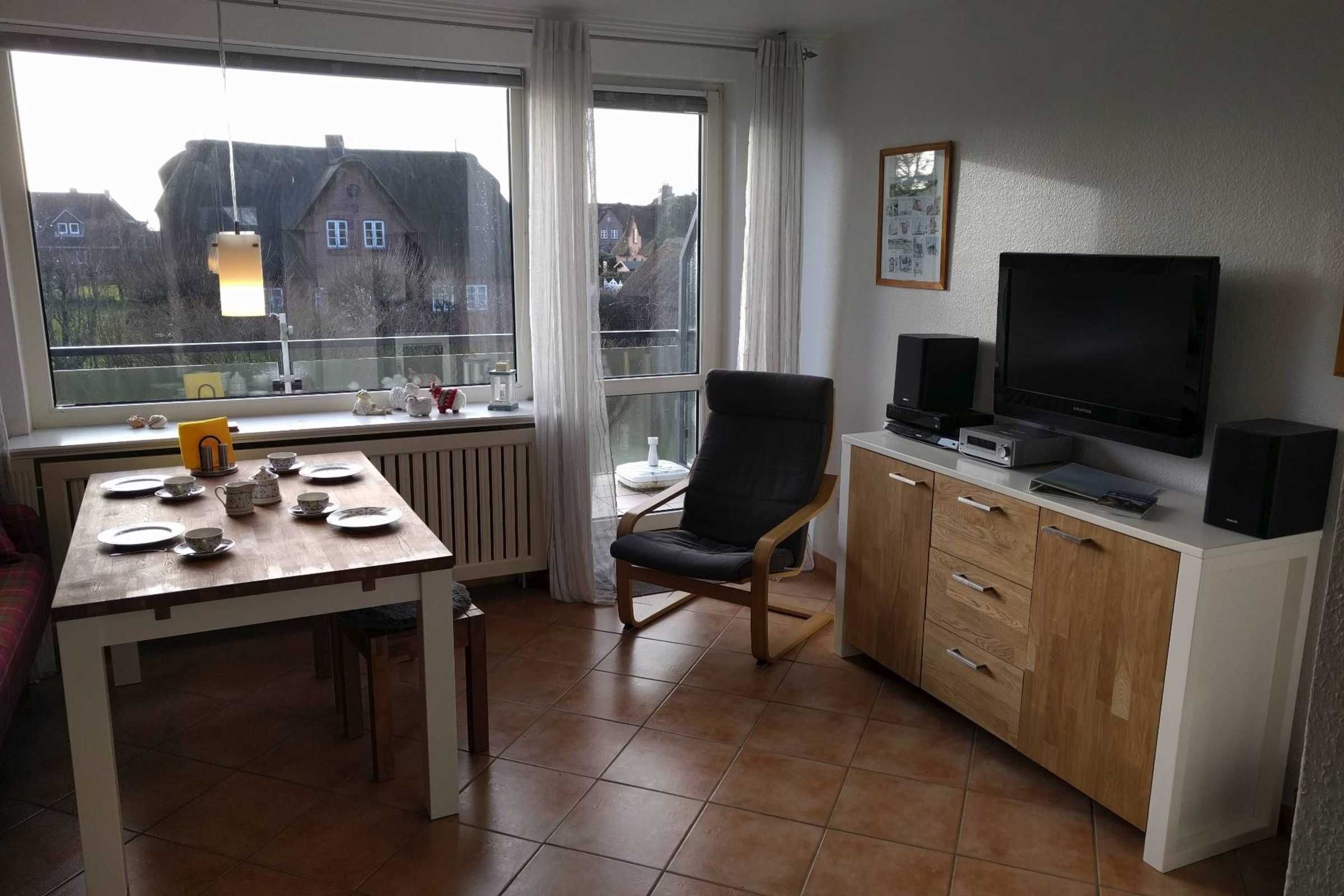 A dining area with a table set for four, a chair, a TV, and speakers on a cabinet.