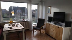 Un coin repas avec une table dressée pour quatre personnes, une chaise, un téléviseur et des haut-parleurs placés sur un meuble.