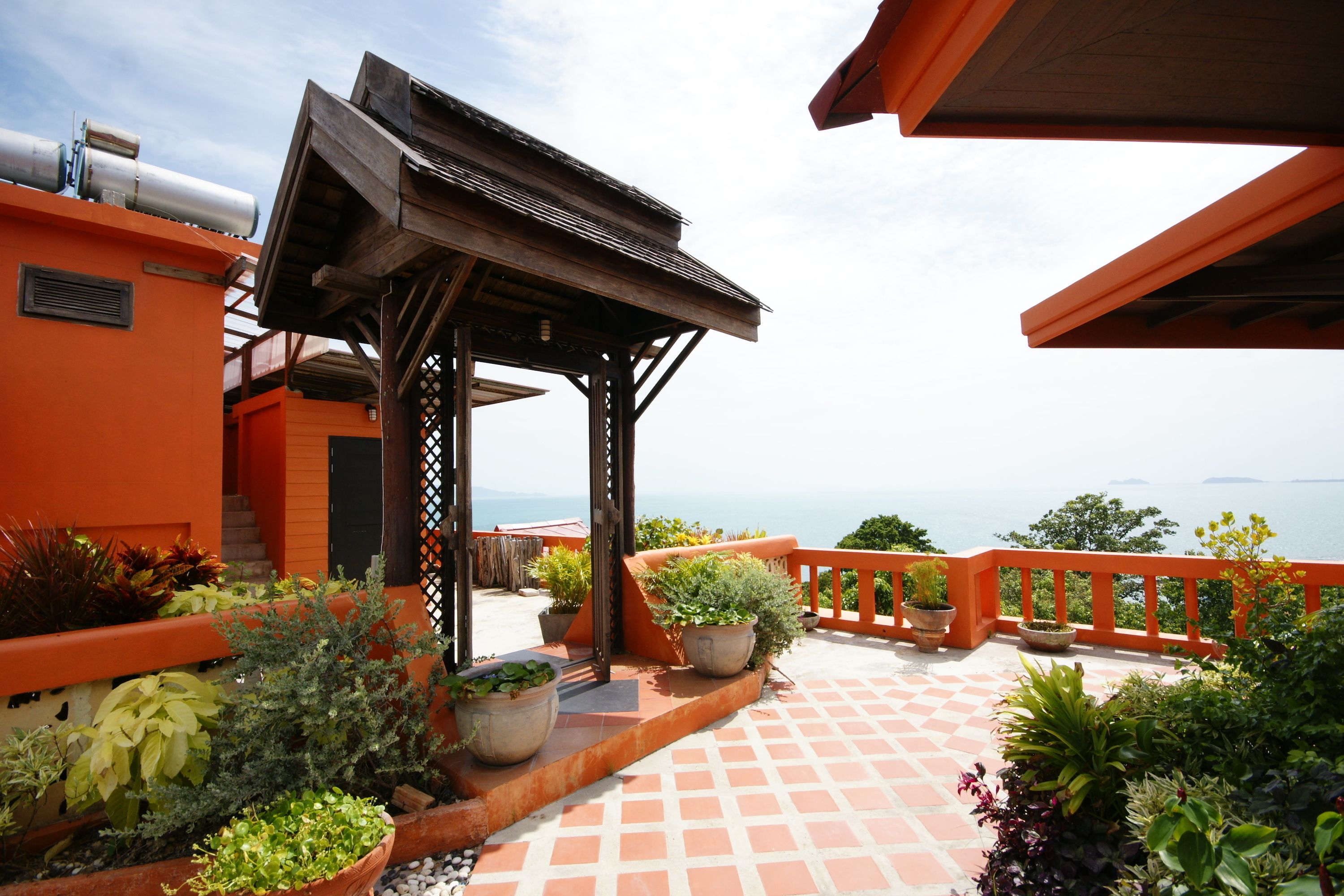 A rooftop terrace with a wooden pergola, potted plants, and a view of the sea.