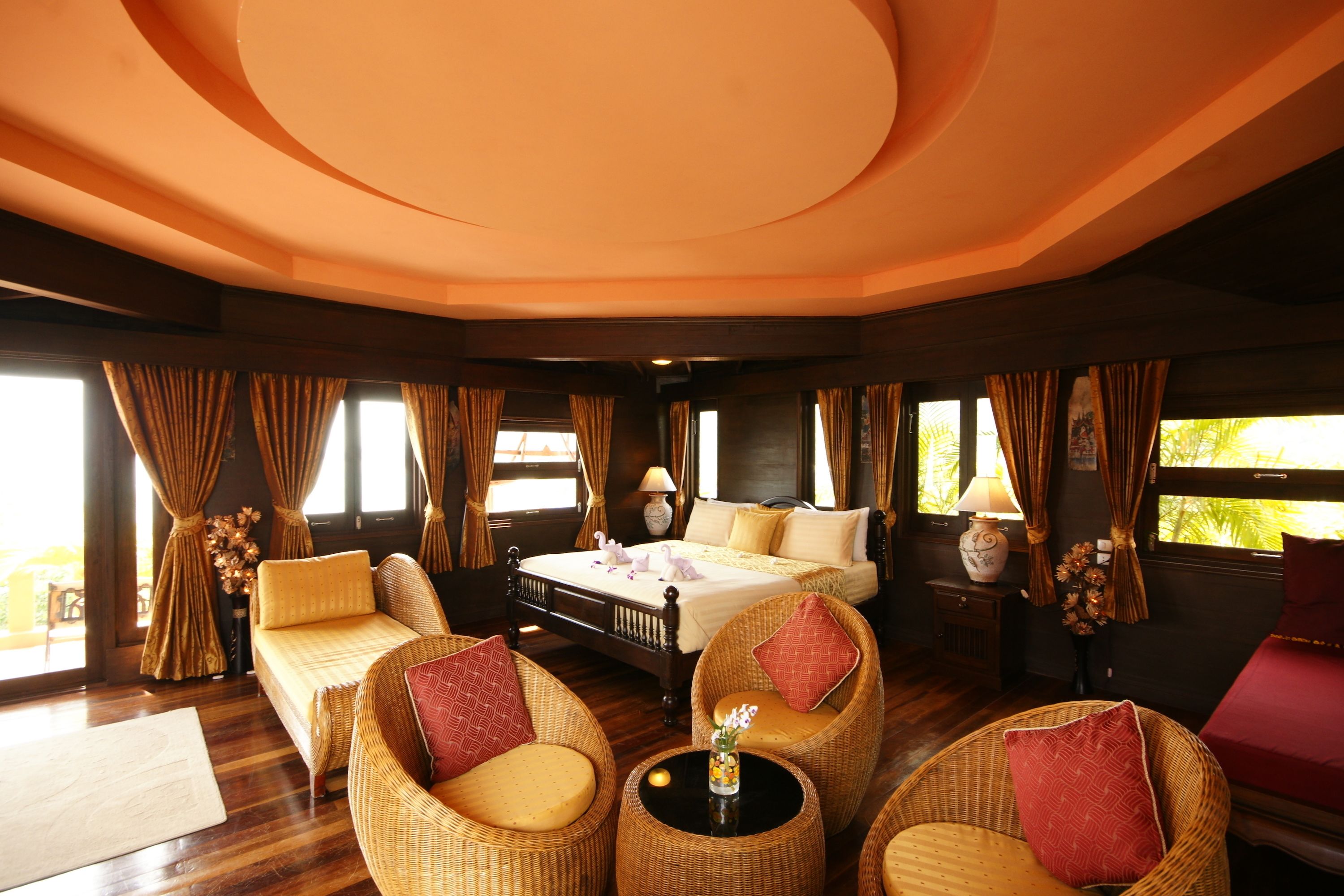 A room with a bed, two wicker chairs, a small table, and a window with curtains.