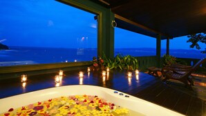 A room with a large bathtub filled with flower petals, a view of the ocean, and several candles on the floor. - Sea Breeze Resort (Ko Pha-ngan)
