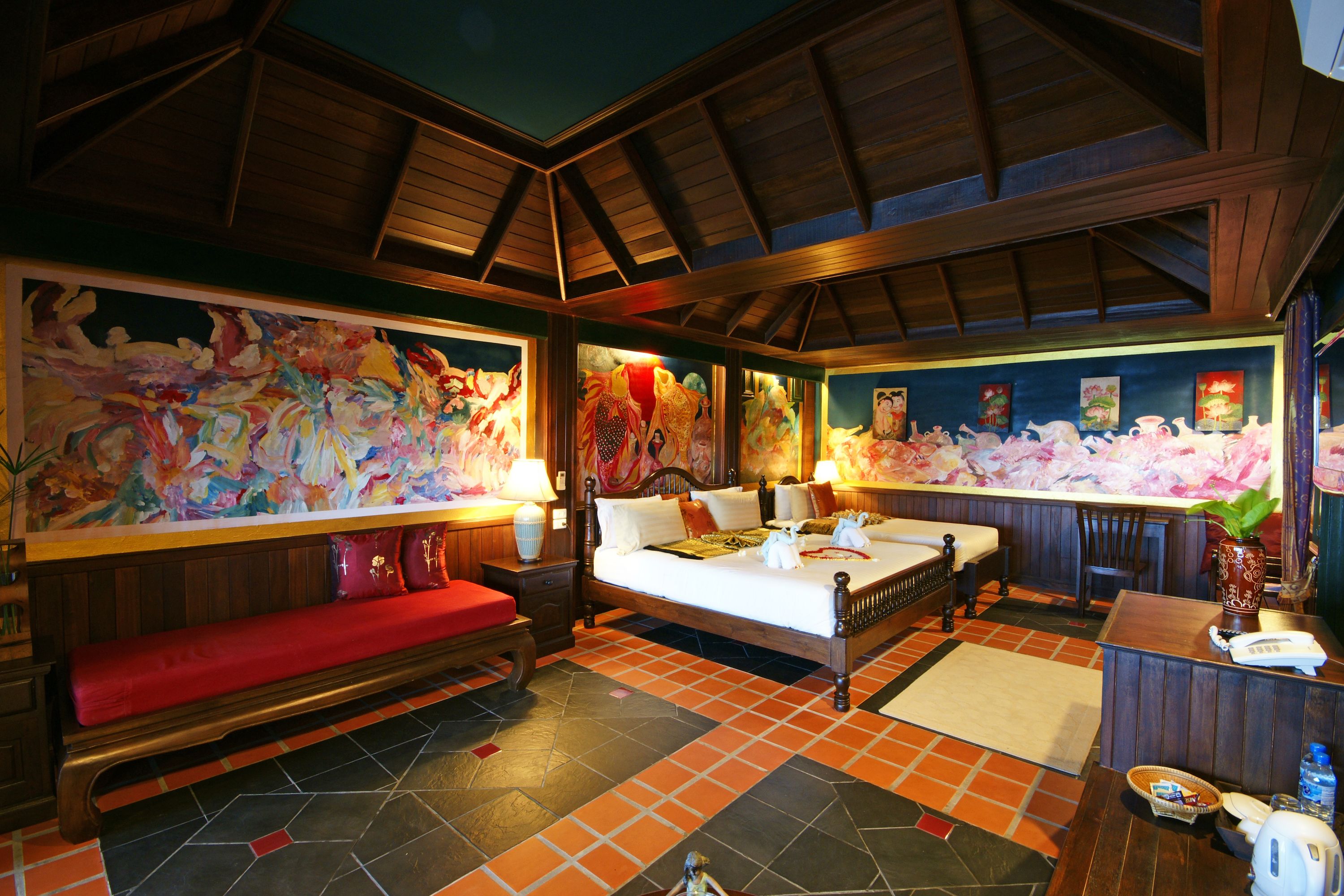 Una habitación con una cama, un banco, un escritorio y obras de arte en las paredes.