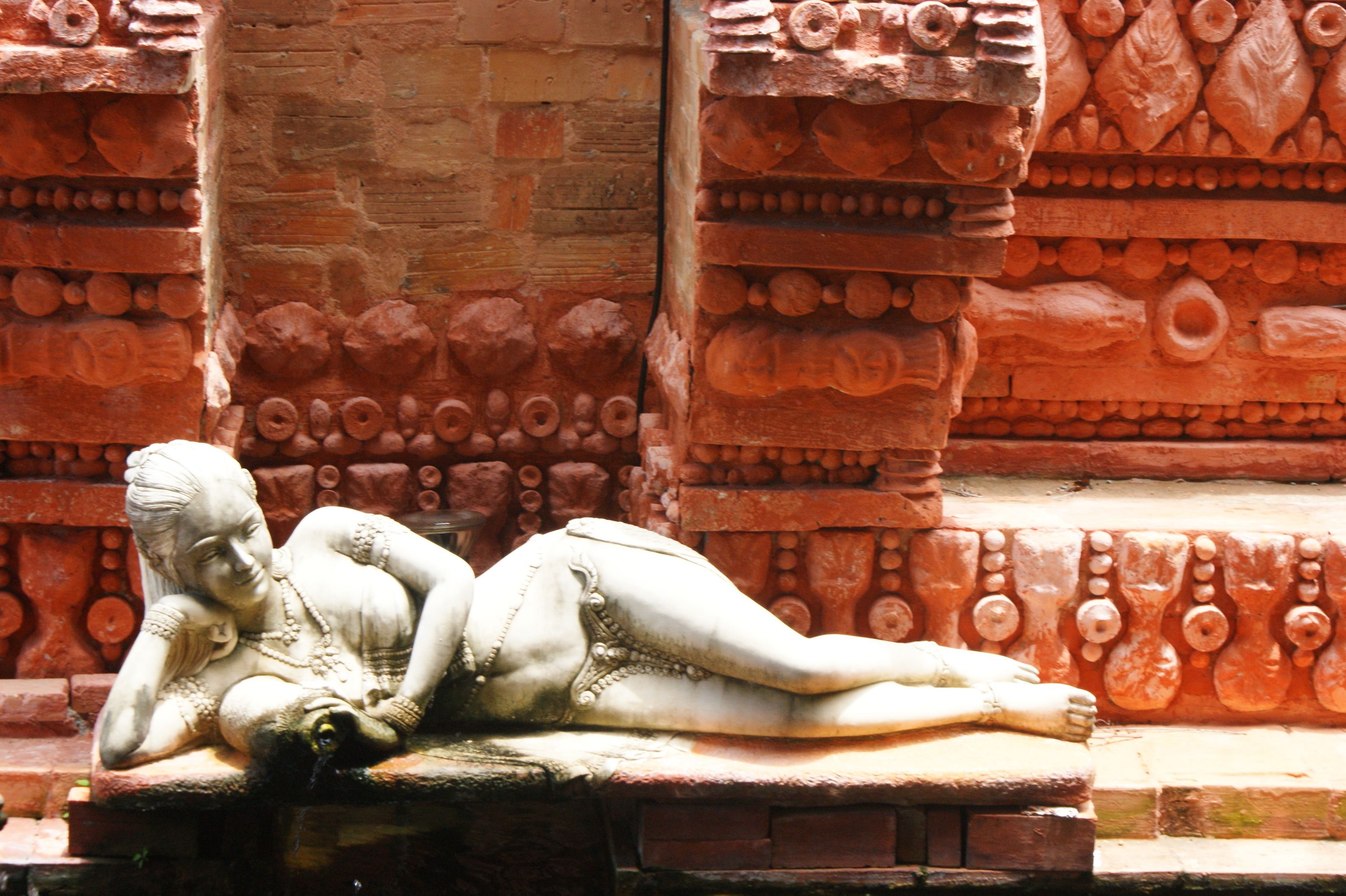 A stone sculpture of a reclining figure on a ledge, set against a backdrop of detailed brickwork.