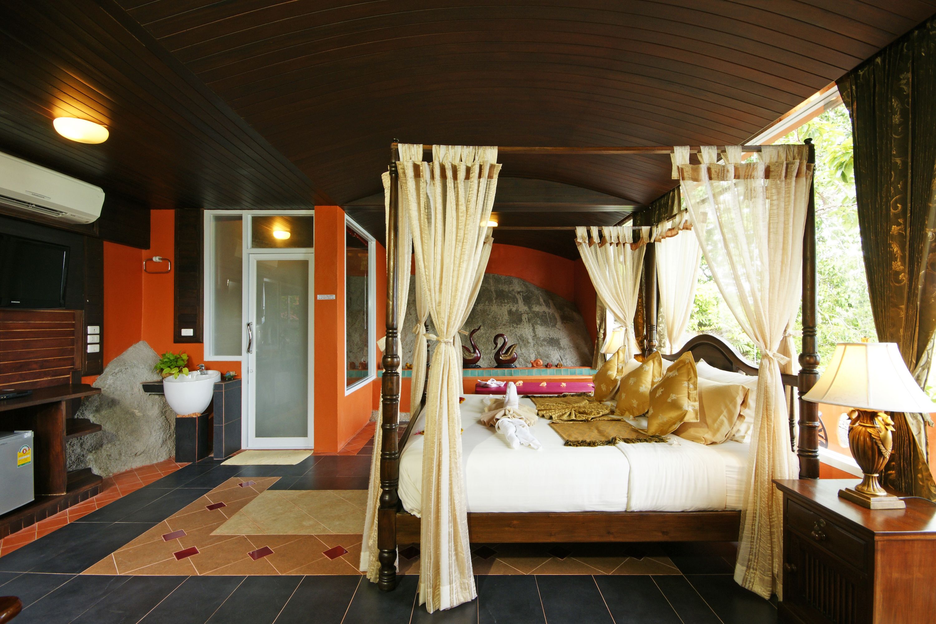Un dormitorio con cama con dosel, una zona de estar con sofá y mesa de centro, y vistas al exterior.