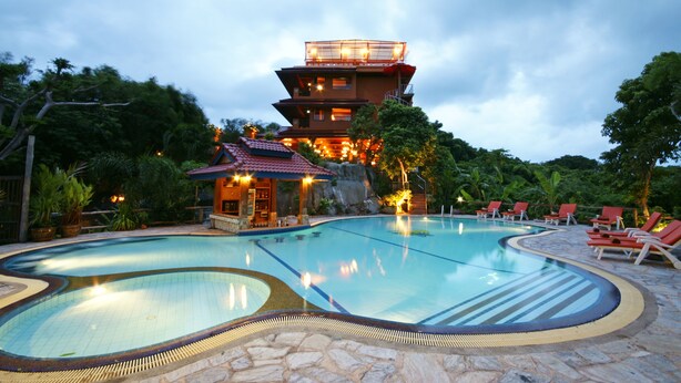 A swimming pool with a stone border, a multi-level building with a red roof, and red lounge chairs around the pool. - Sea Breeze Resort (Ko Pha-ngan)