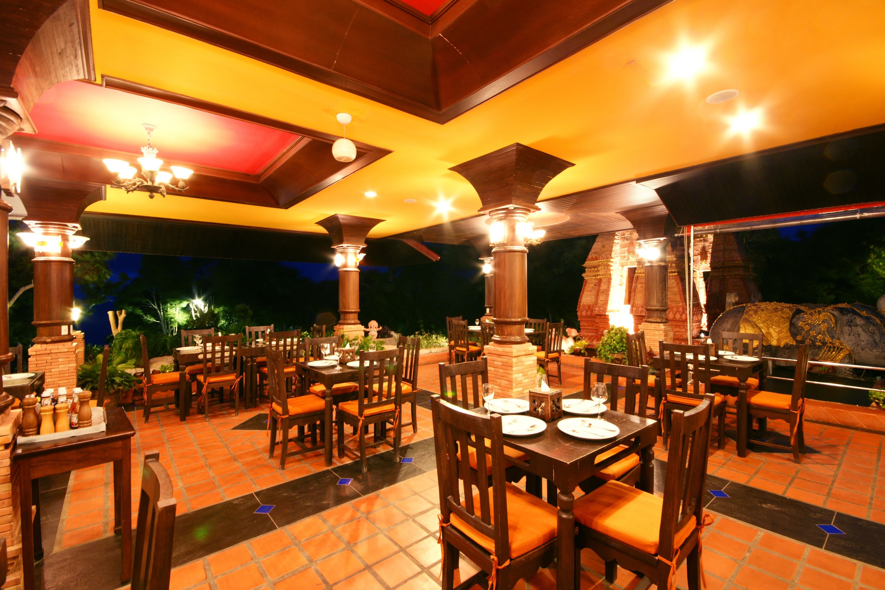 An outdoor restaurant with wooden tables and chairs, a tiled floor, and a stone fireplace.