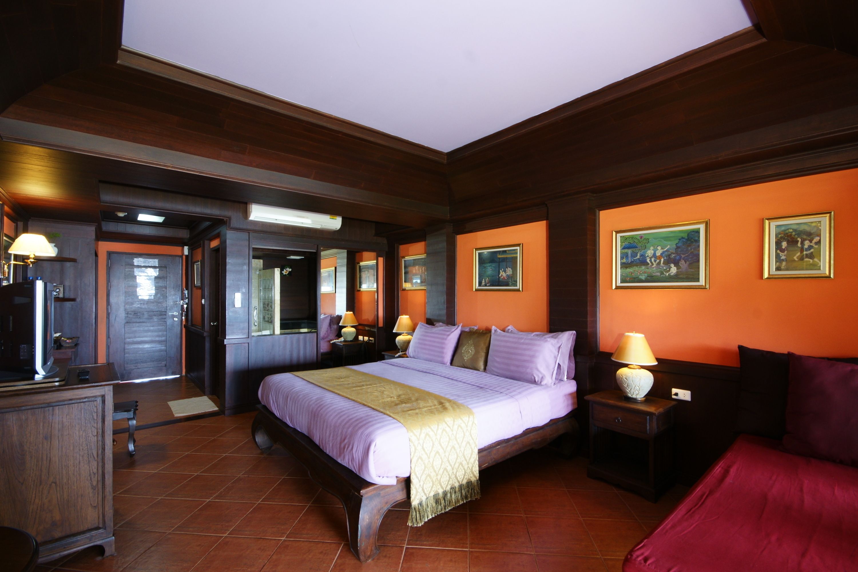 Habitación de hotel con una cama grande, un escritorio y una silla. Hay dos mesitas de noche con lámparas. La habitación tiene paneles de madera en las paredes y el techo.