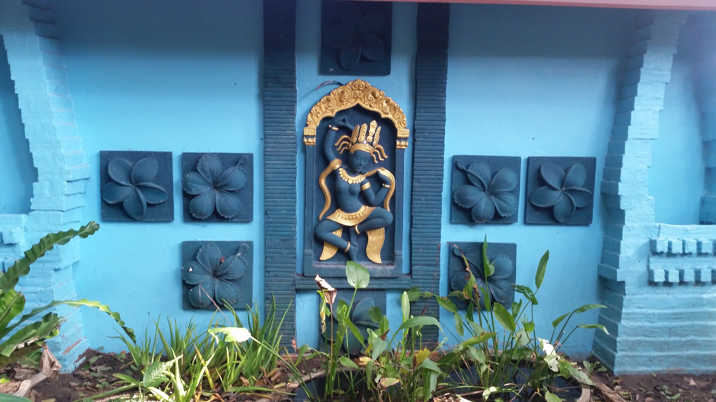 A blue wall with a central relief sculpture of a deity, surrounded by four flower-shaped panels.