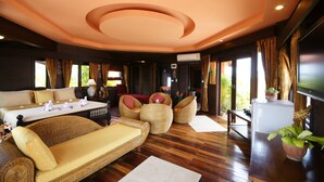 A spacious room with a large bed, a sofa, and a dining table. There are wicker chairs and a small table with a plant. The room has wooden flooring and a ceiling with a circular design. - Sea Breeze Resort (Ko Pha-ngan)